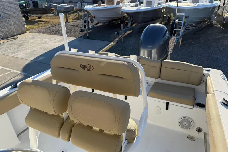 Slide: The Image of 2018 Sea Hunt Ultra 225 boat interior with beige seating and motor, parked outdoors. - 18