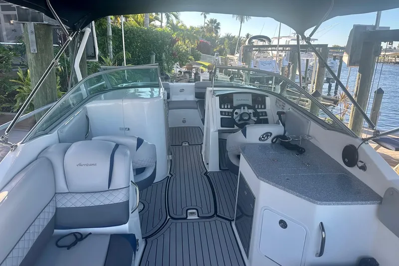 Slide: The Image of 2019 Hurricane SunDeck 2690 OB boat interior with seating and helm, docked by the water. - 2