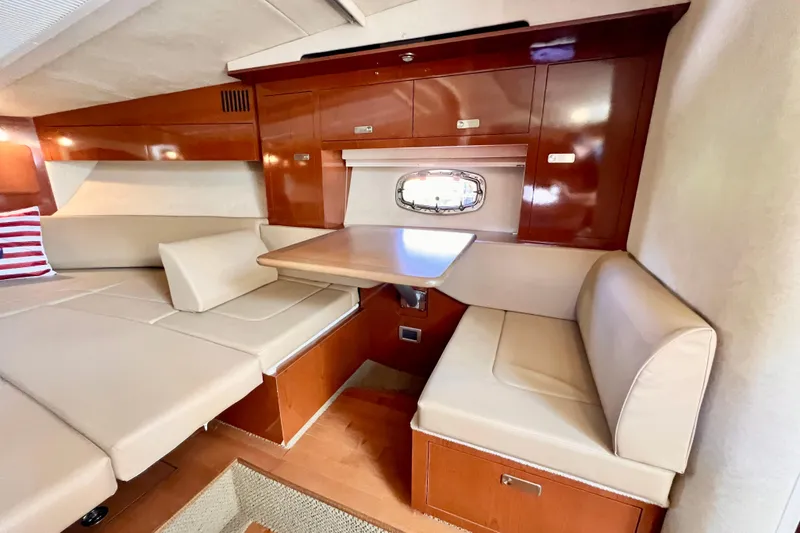Slide: The Image of 2012 Sea Ray 310 Sundancer cabin with beige seating, wooden cabinetry, and a small dining table. - 21