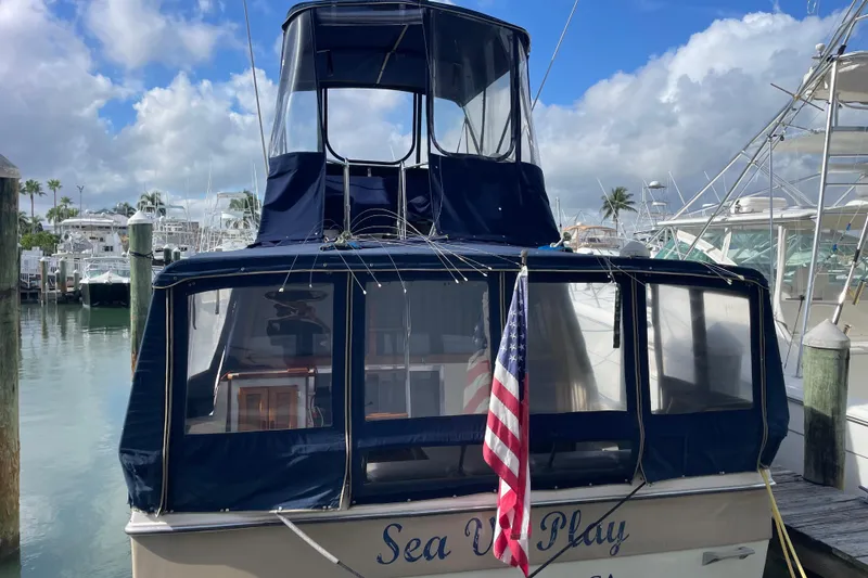 Slide: The Image of 1983 Bayliner 3270 Explorer docked, featuring blue canopy and American flag. - 6
