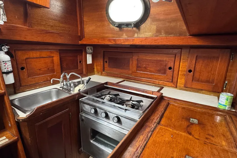 Slide: The Image of 1977 Westsail Cutter kitchen with wooden cabinets, stainless steel stove, and sink. - 10