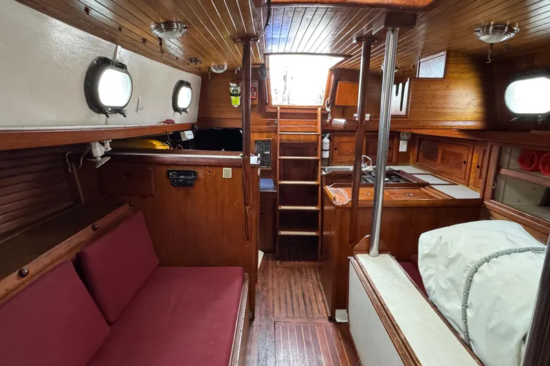 Slide: The Image of 1977 Westsail Cutter interior with wooden finish, red cushions, and compact kitchen area. - 17