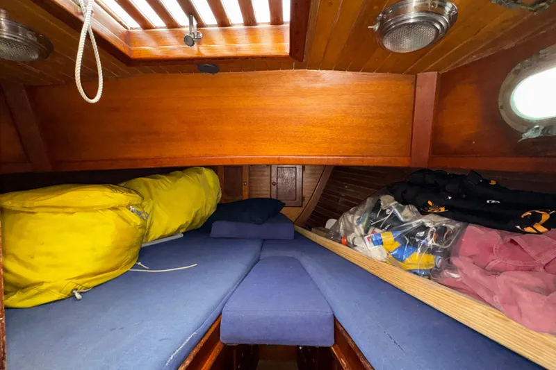 Slide: The Image of 1977 Westsail Cutter cabin interior with blue cushions, wooden paneling, and storage space. - 27