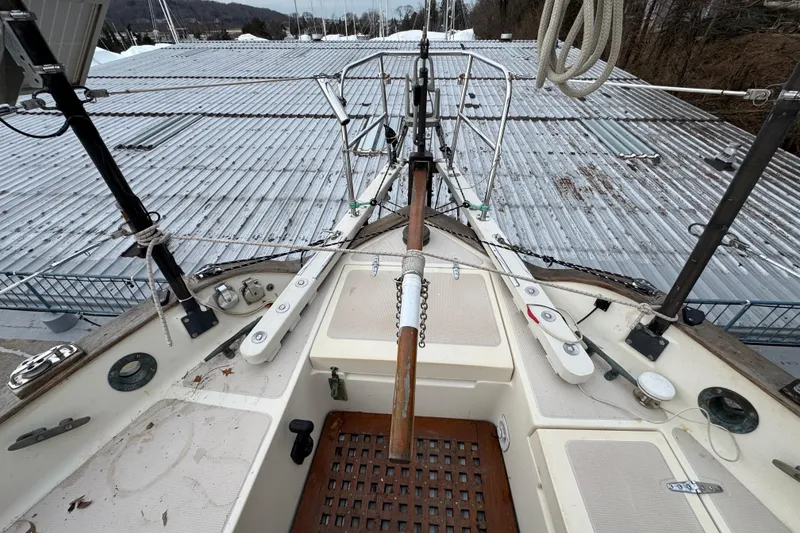 Slide: The Image of 1977 Westsail Cutter sailboat deck with rigging and equipment, docked near metal roofing. - 32