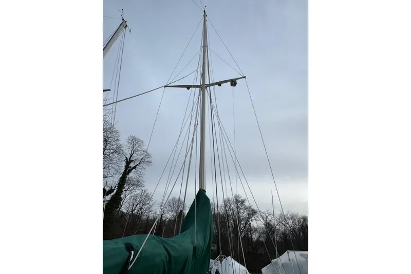 Slide: The Image of 1977 Westsail Cutter sailboat mast against cloudy sky, surrounded by trees. - 35