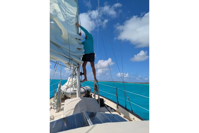 Slide: The Image of Person adjusting sails on 1977 Westsail Cutter under clear blue sky. - 45