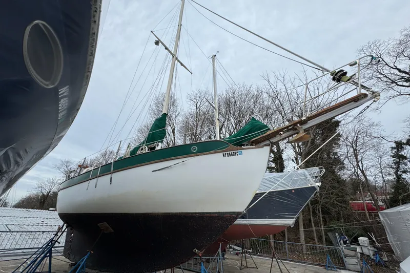 Slide: The Image of 1977 Westsail Cutter sailboat on dry dock, surrounded by trees and other boats. - 46