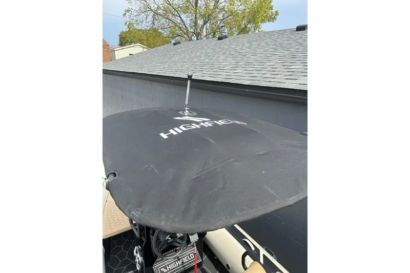 Slide: The Image of 2024 Highfield Sport 560 boat cover with logo, near a gray shingled roof. - 11