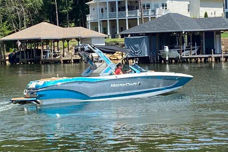 The Image of 2022 MasterCraft X24 boat cruising on a lake near waterfront homes. - 0