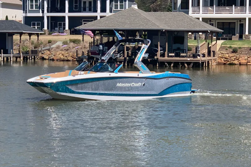 Slide: The Image of 2022 MasterCraft X24 boat cruising on a lake near waterfront homes. - 3