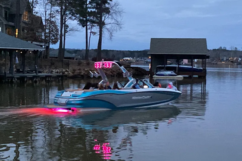 Slide: The Image of 2022 MasterCraft X24 boat cruising on a calm lake at dusk with vibrant lights. - 4