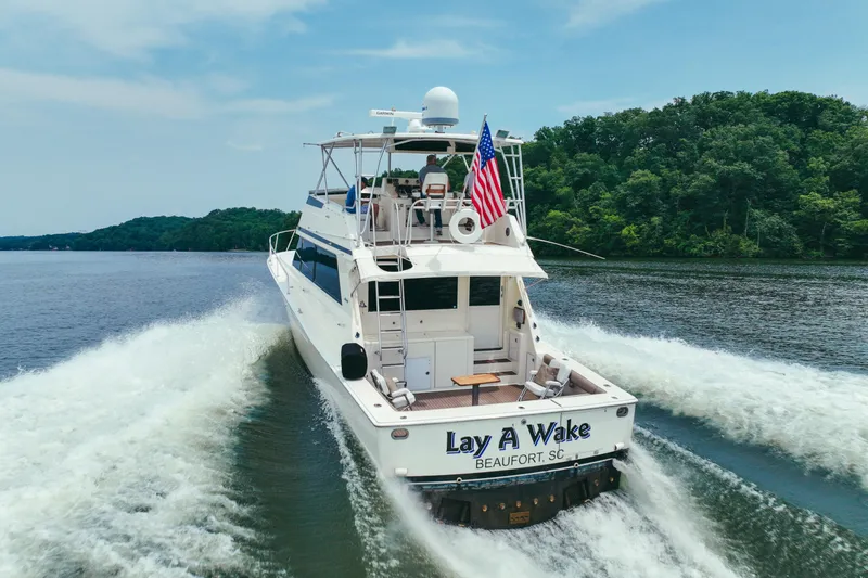 The Image of 1990 Viking 53 Convertible yacht cruising on a scenic river with lush green trees. - 0