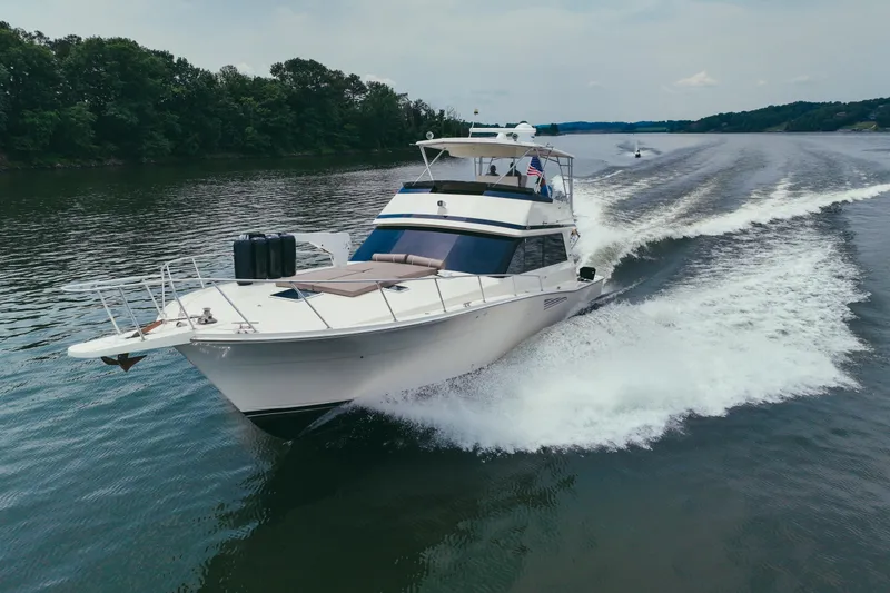 Slide: The Image of 1990 Viking 53 Convertible yacht cruising on a serene lake with lush green shoreline. - 2