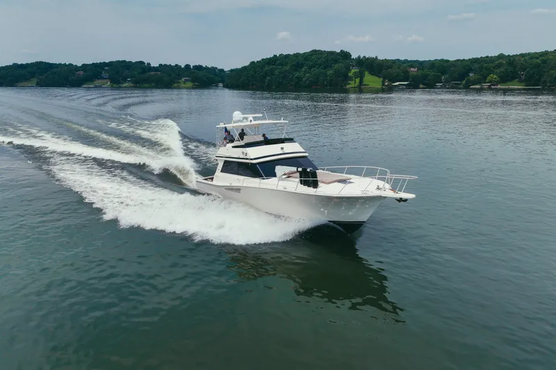 Slide: The Image of 1990 Viking 53 Convertible yacht cruising on a serene lake with lush green shoreline. - 5