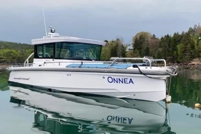 The Image of 2022 Axopar 28 Cabin boat on calm water near a forested shoreline. - 0