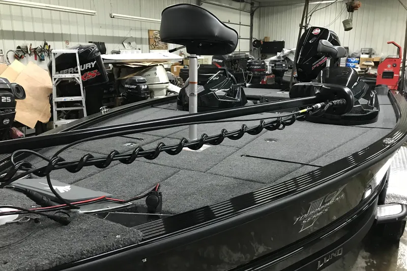 Slide: The Image of 2026 Lund 1875 Pro-V Bass XS boat in a workshop, featuring advanced fishing equipment. - 7