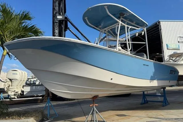 Slide: The Image of 2024 Carolina Skiff 22 Ultra Elite boat on stands, blue and white hull, marina background. - 2
