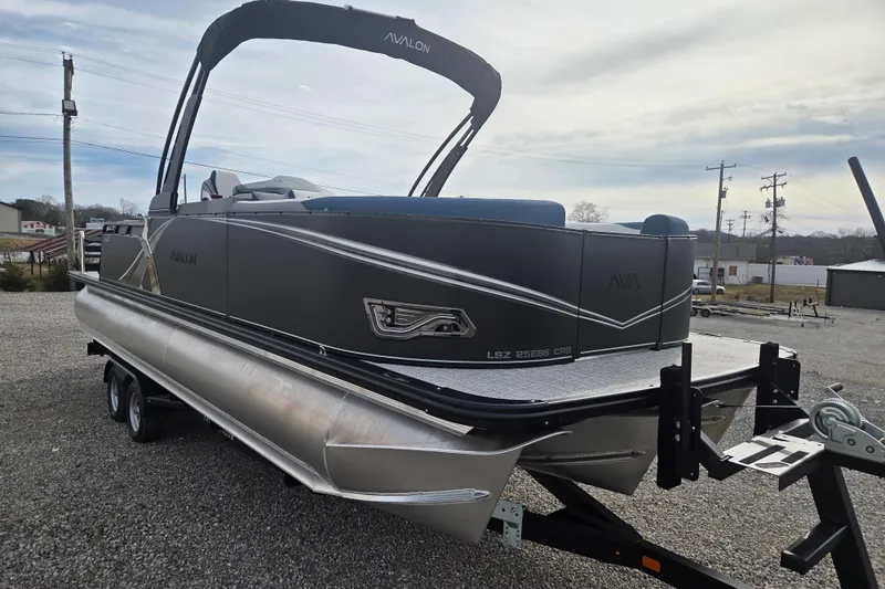 Slide: The Image of 2026 Avalon Platinum LSZ 2585 Cruise Rear Bench pontoon boat on trailer, parked outdoors. - 2