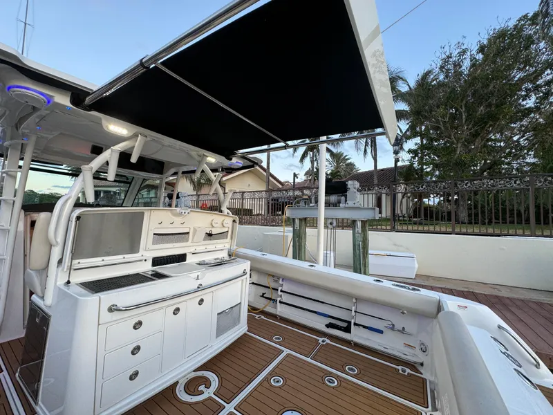 Slide: The Image of 2017 Boston Whaler 370 Outrage boat with outdoor kitchen and canopy, docked near a house. - 17