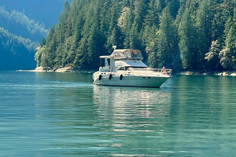 Slide: The Image of 2000 Sea Ray 420 Aft Cabin yacht on serene lake with forested backdrop. - 28
