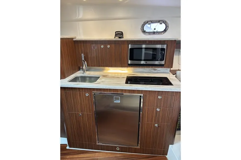 Slide: The Image of 2023 Pursuit OS 355 Offshore yacht kitchen with wood cabinetry, sink, microwave, and stovetop. - 21