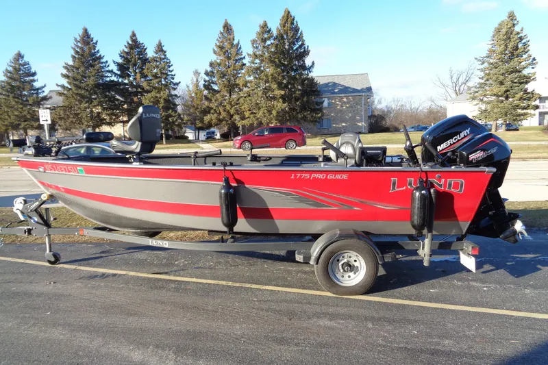 The Image of 2021 Lund 1775 Pro Guide boat on trailer, red and gray, parked outdoors. - 0