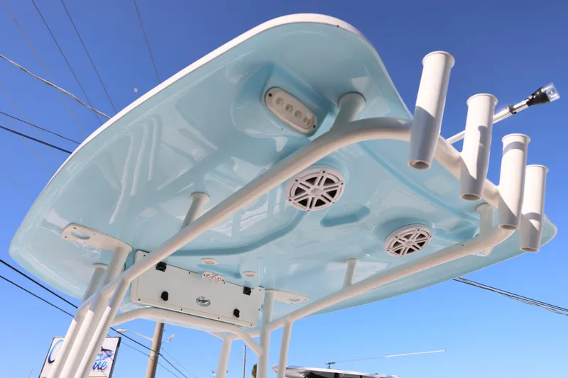 Slide: The Image of 2022 Tidewater 220 CC Adventure boat T-top with rod holders and speakers against blue sky. - 10