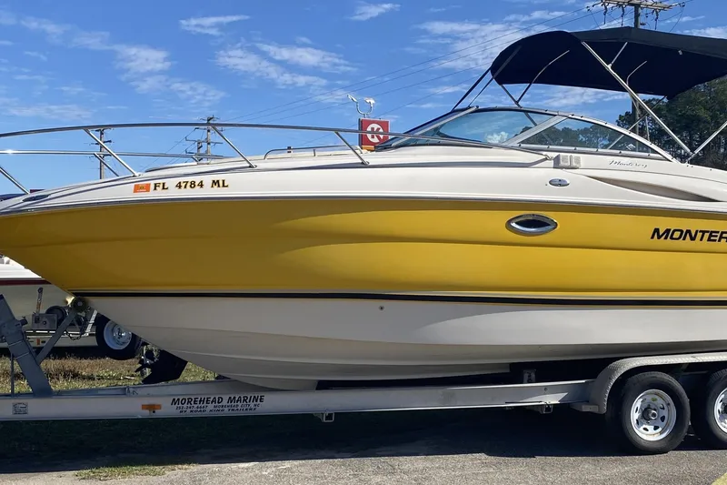The Image of 2004 Monterey 245 Cruiser boat with yellow hull on trailer, under clear blue sky. - 1