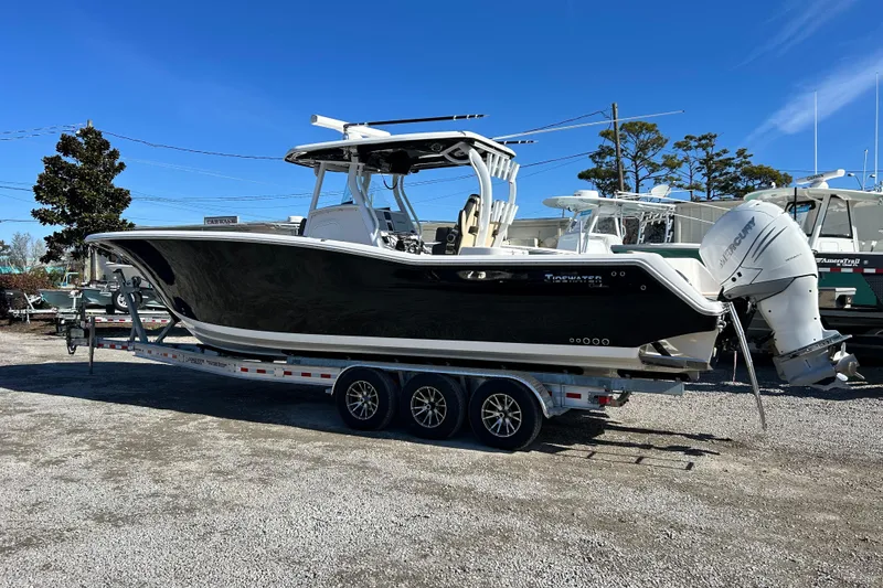 Slide: The Image of 2020 Tidewater 320 CC Adventure boat on trailer, parked outdoors under clear blue sky. - 3