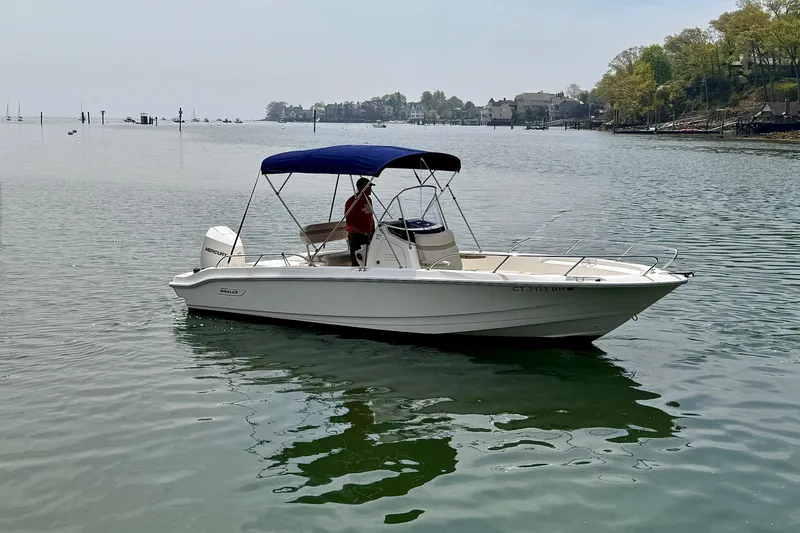 Slide: The Image of 2022 Boston Whaler 220 Dauntless boat on calm water with blue canopy. - 1