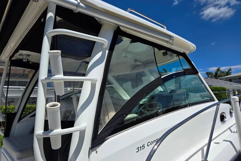 Slide: The Image of 2016 Boston Whaler 315 Conquest boat exterior with rod holders and windshield, under clear blue sky. - 3