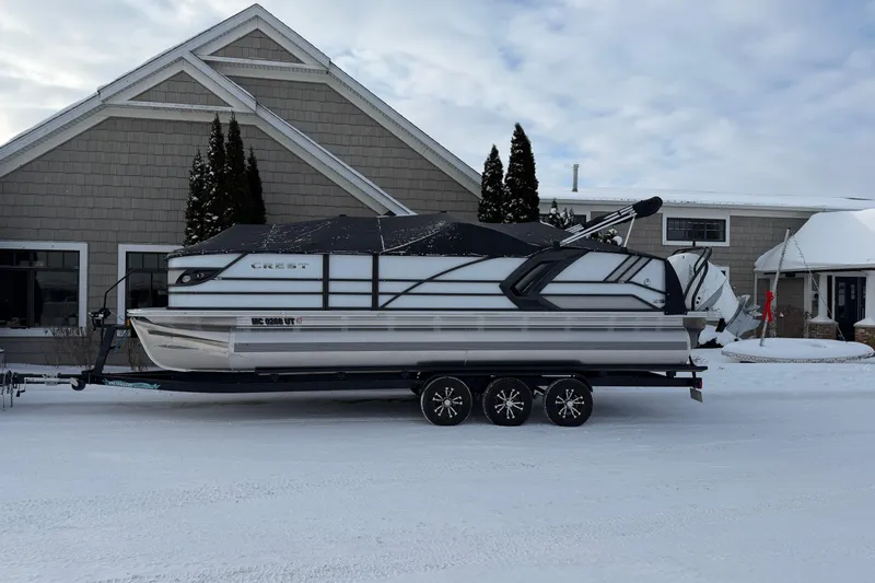 The Image of 2022 Crest Continental 250 SLS pontoon boat on trailer in snowy setting. - 0