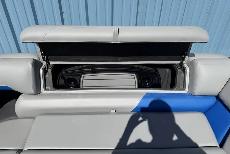 Slide: The Image of 2026 Sun Tracker Party Barge 20 DLX storage compartment with open lid, blue and gray seating. - 14