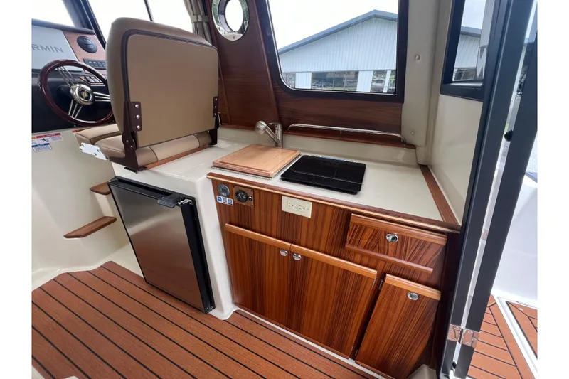 Slide: The Image of 2025 Ranger Tugs R-25 interior with kitchenette, wood cabinetry, and compact fridge. - 12