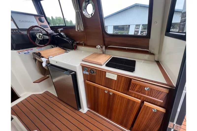 Slide: The Image of 2025 Ranger Tugs R-25 interior with wood finish, kitchenette, and steering area. - 13