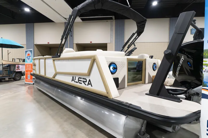 Slide: The Image of 2026 Alera M23Q pontoon boat displayed indoors with modern design and Mercury engine. - 17