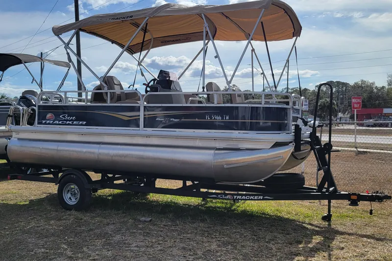 The Image of 2024 Sun Tracker Bass Buggy 18 DLX pontoon boat on trailer, parked outdoors. - 1