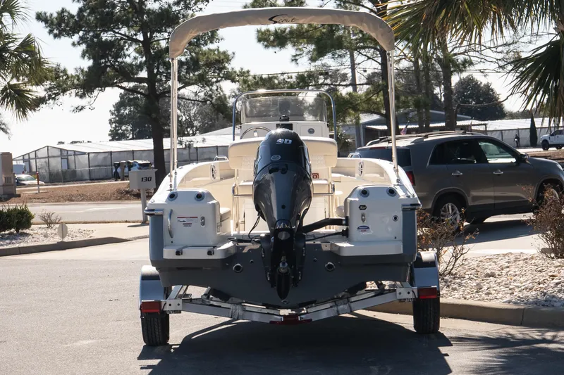 Slide: The Image of 2026 Scout 188 Sportfish boat on trailer, parked outdoors with trees and vehicles nearby. - 5