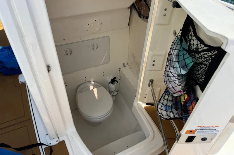 Slide: The Image of 2021 Robalo R242 Center Console boat interior with compact marine toilet and storage net. - 17