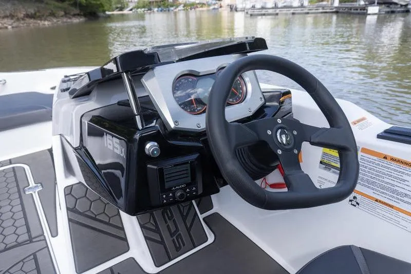 Slide: The Image of 2026 Scarab 165 LX boat dashboard with steering wheel and gauges on a lake. - 9