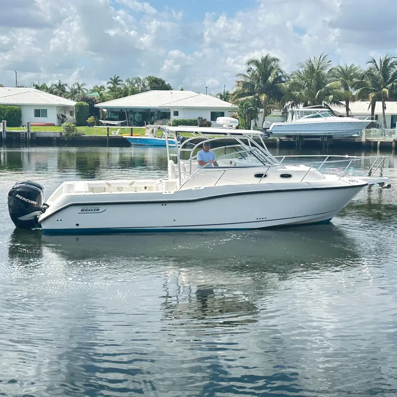 Slide: The Image of 2006 Boston Whaler 305 Conquest boat on calm water, surrounded by palm trees and houses. - 3