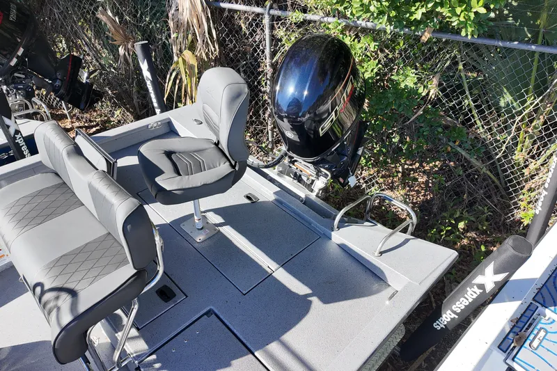 Slide: The Image of 2026 Xpress H20B Bay boat with seating and outboard motor, parked near a fence. - 13