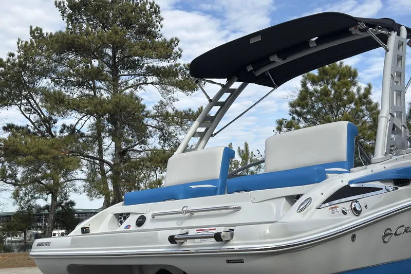 Slide: The Image of 2026 Crownline 220 SS boat with blue seating and canopy, parked near trees. - 5