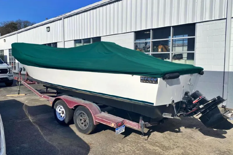 Slide: The Image of 1976 Aquasport 24 Launch boat on trailer, covered with green tarp, parked outside a building. - 2