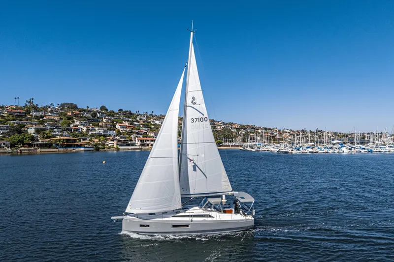 Slide: The Image of 2025 Beneteau Oceanis 37.1 sailing near a coastal marina under clear blue skies. - 47