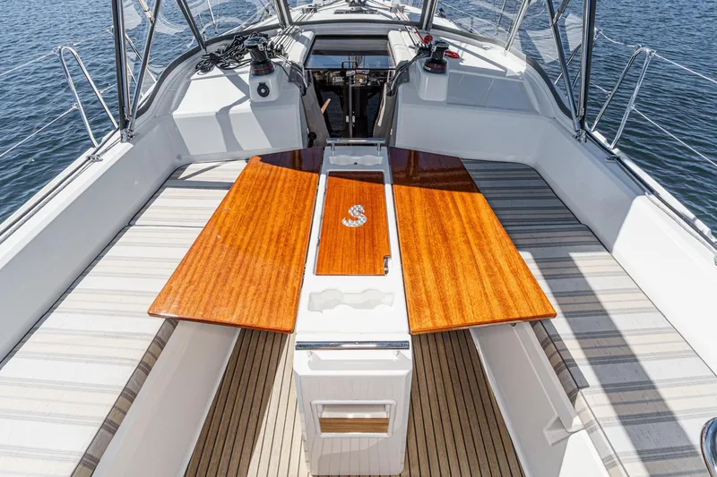 Slide: The Image of 2025 Beneteau Oceanis 37.1 yacht cockpit with wooden table and seating, on calm water. - 60