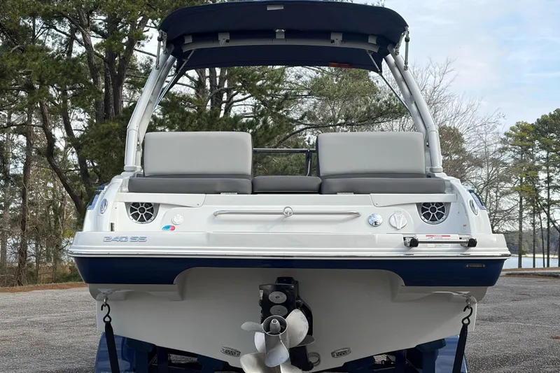 Slide: The Image of 2026 Crownline 240 SS boat, rear view, parked outdoors with trees in background. - 12