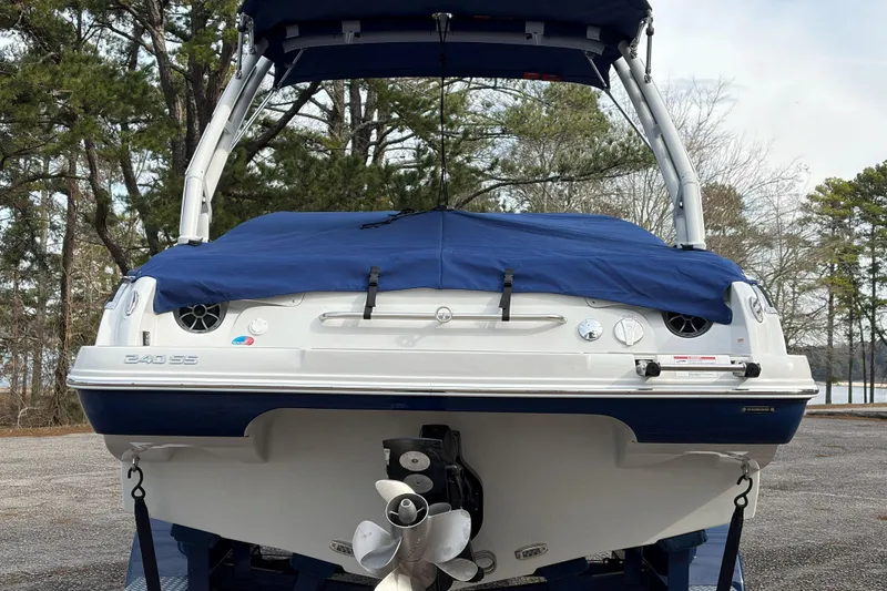Slide: The Image of 2026 Crownline 240 SS boat with blue cover, parked near a lake and trees. - 2
