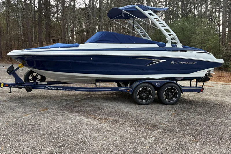 Slide: The Image of 2026 Crownline 240 SS boat on trailer, parked in wooded area. - 3