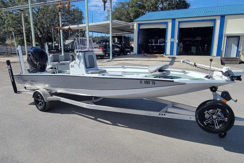 The Image of 2024 Xpress H22B Bay boat on trailer, parked outdoors near blue-roofed building. - 1